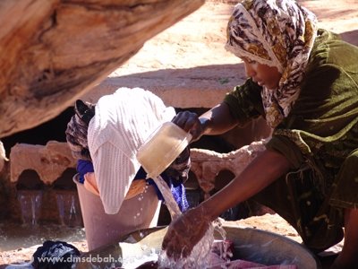 Une femme lavant son linge directement dans l'eau de la Foggara, avant répartition.